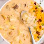 overhead view of creamy potato soup in a bowl, topped with crispy bacon, shredded cheese, and chives