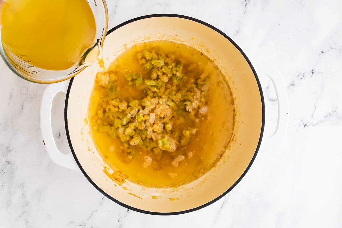 overhead view of chicken broth being whisked into the pot with seasonings