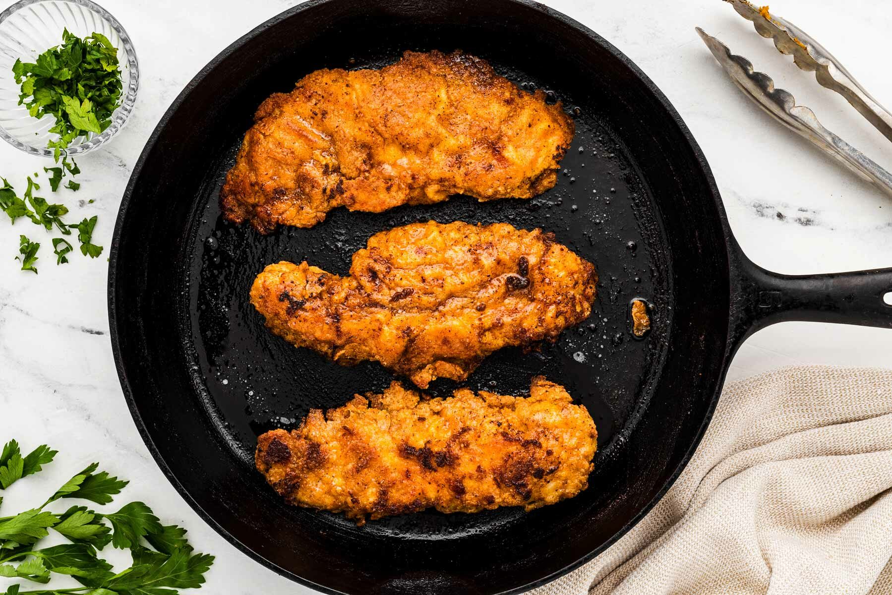 overhead view of three fried chicken pieces in cast iron skillet