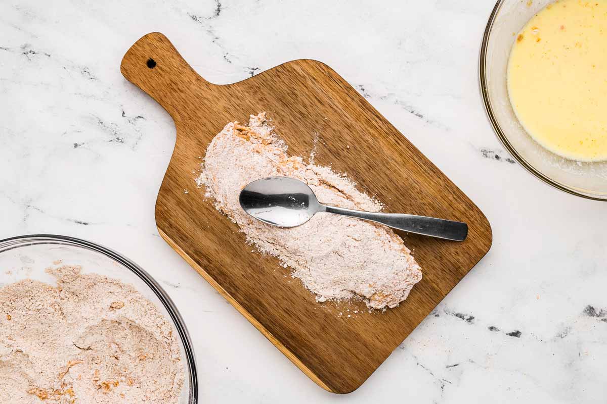 overhead view of raw breaded chicken breast on cutting board with spoon