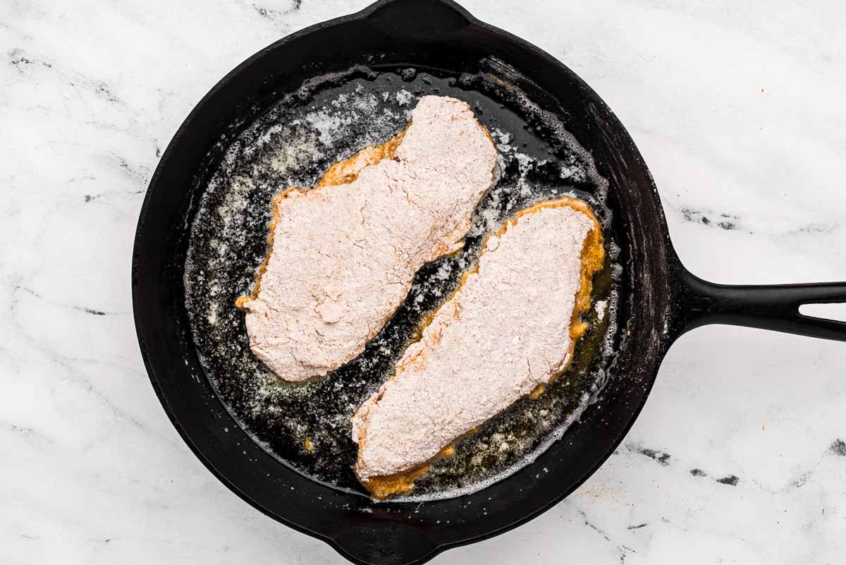 overhead view of two uncooked breaded chicken pieces in cast iron skillet