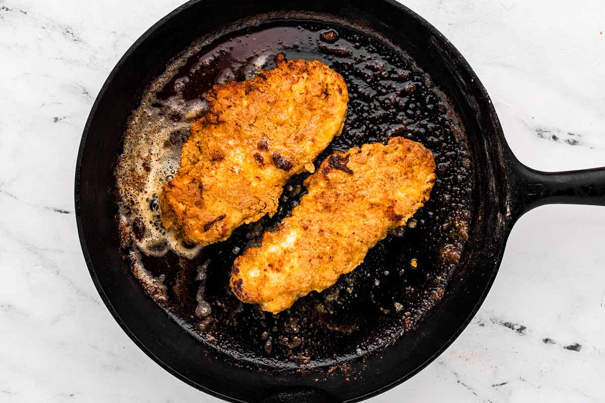 overhead view of two fried chicken pieces in cast iron skillet