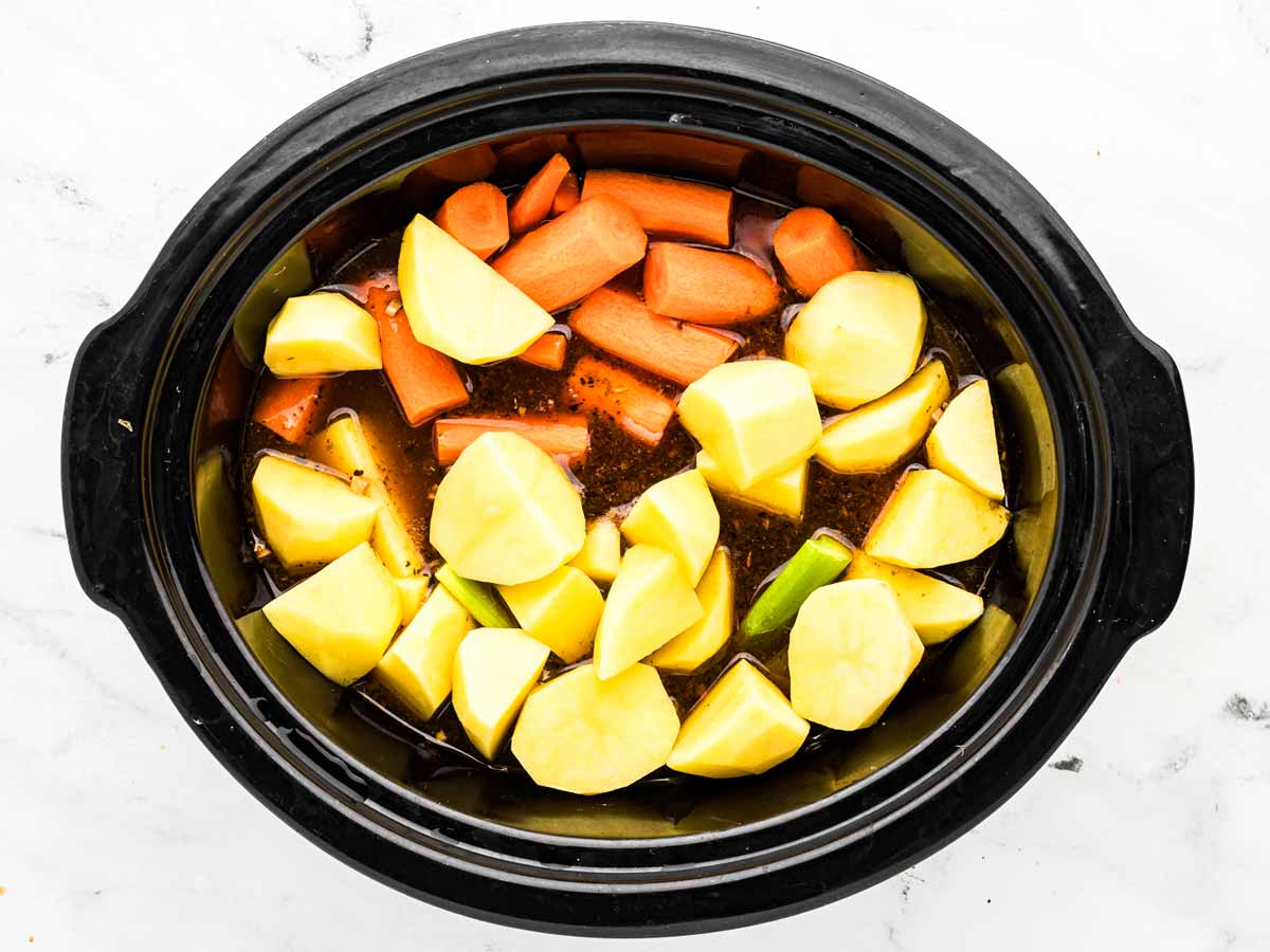 overhead view of potatoes, carrots, and celery being added to crockpot