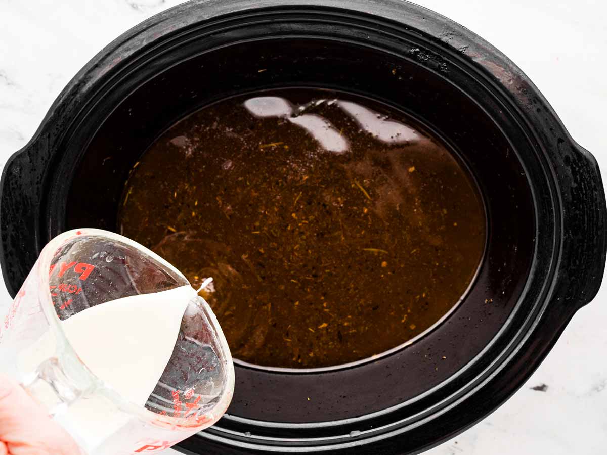 overhead view of cornstarch slurry being added to gravy in crockpot