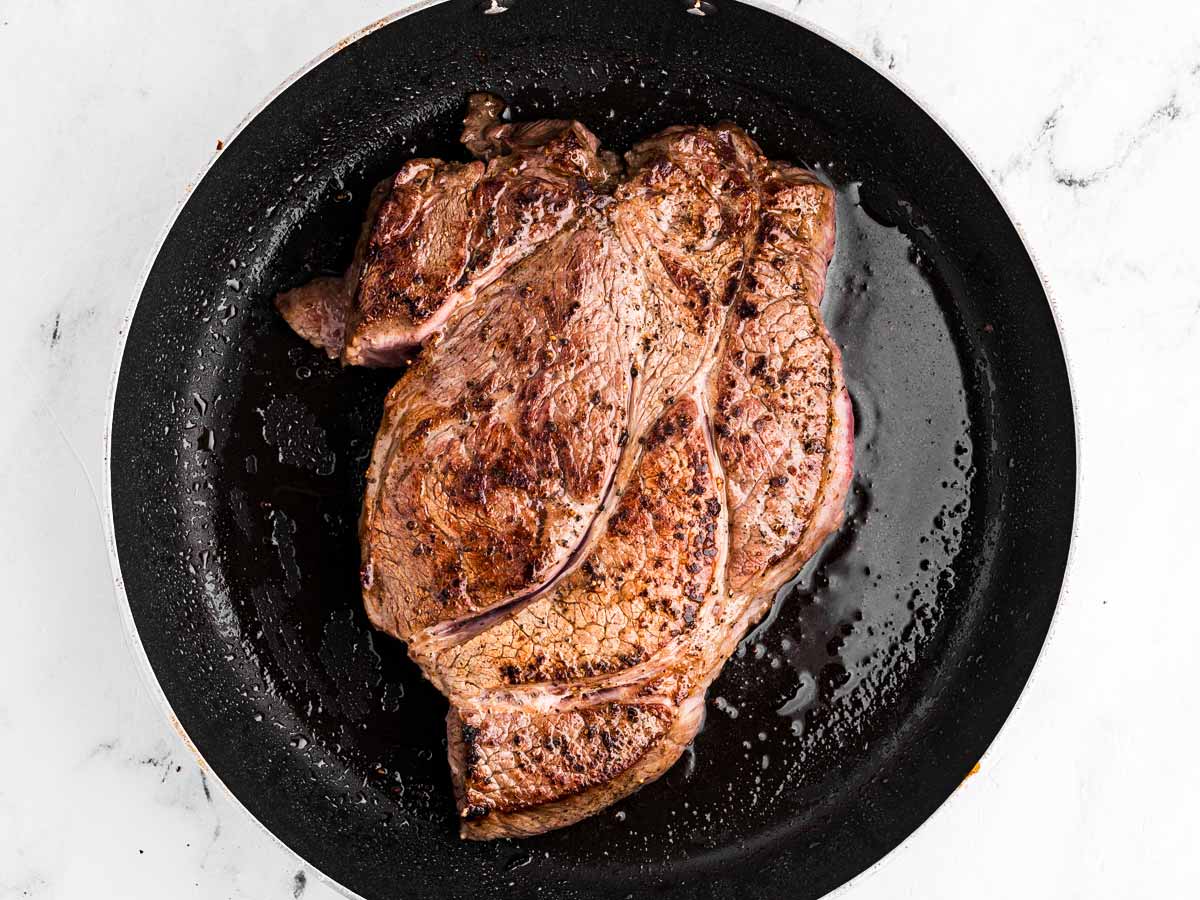 overhead view of chuck roast searing in skillet with oil