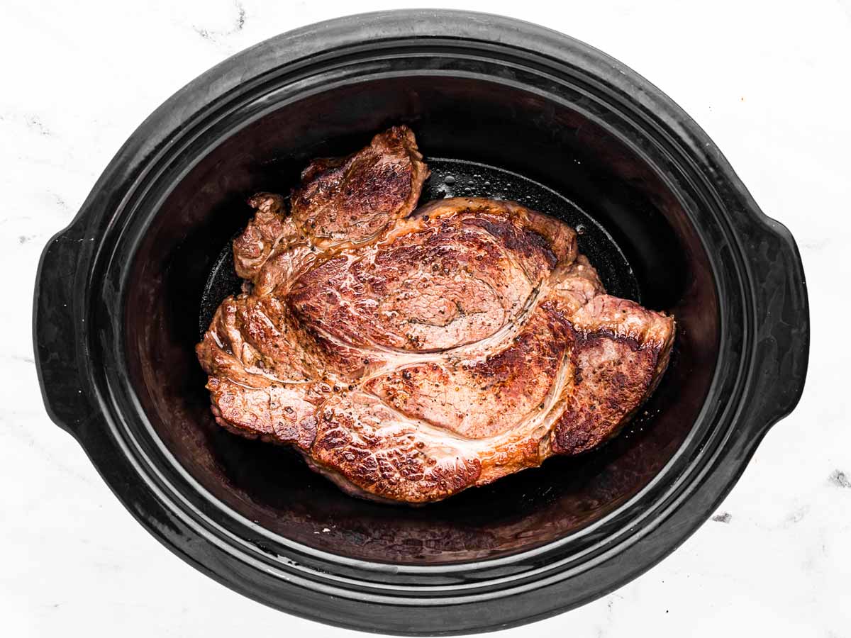 overhead view of seared chuck roast in crockpot with broth