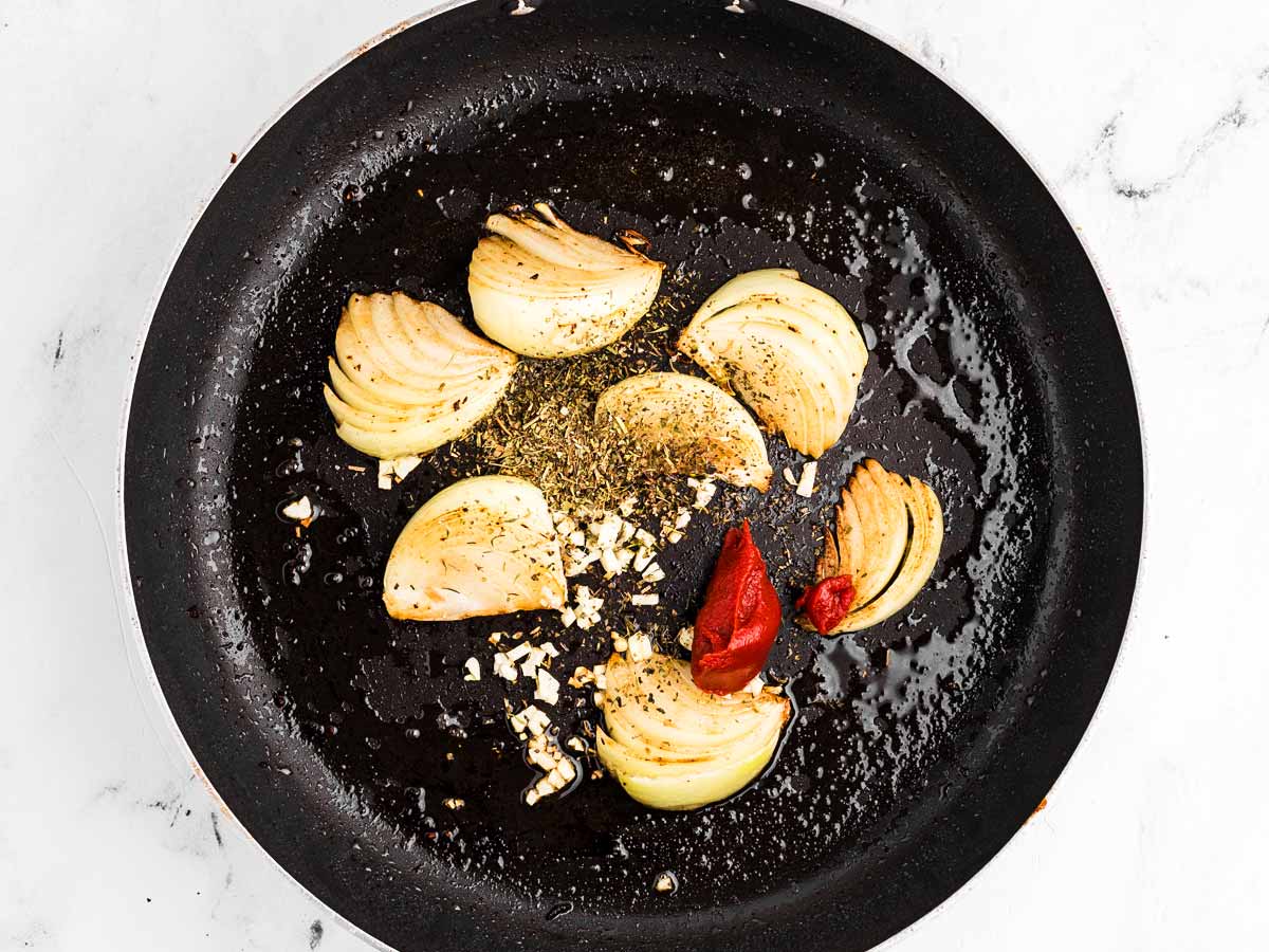 overhead view of onions cooking in skillet with garlic and tomato paste