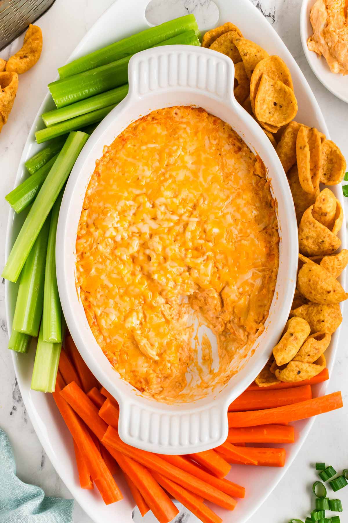 overhead view of buffalo chicken dip in white dish surrounded by chips and vegetables