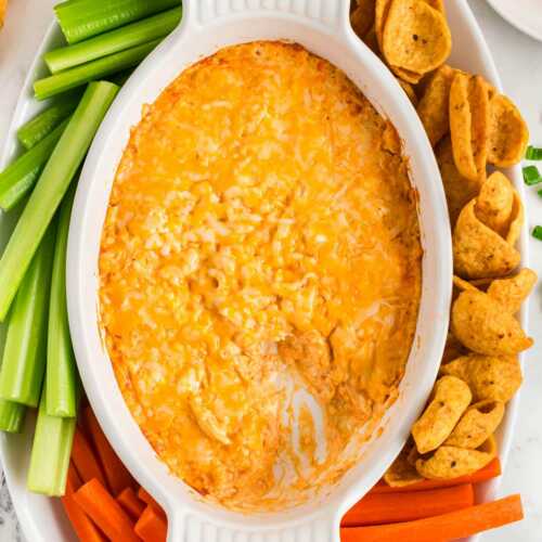 overhead view of buffalo chicken dip in white dish surrounded by chips and vegetables