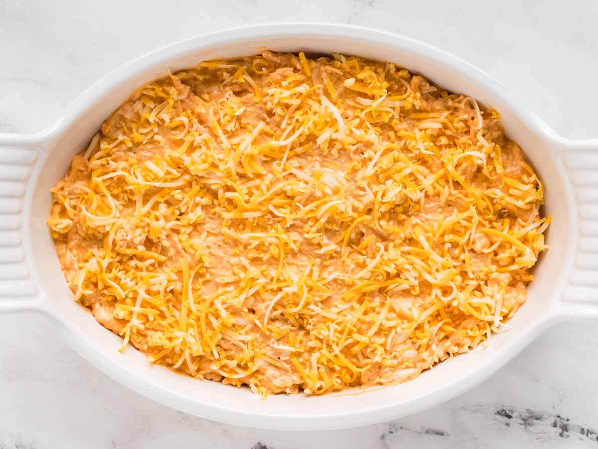 overhead view of unbaked buffalo chicken dip in white dish sprinkled with cheese