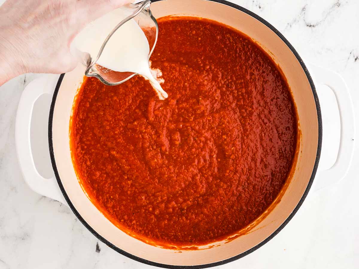 overhead view of heavy cream being poured into blended tomato soup in pot