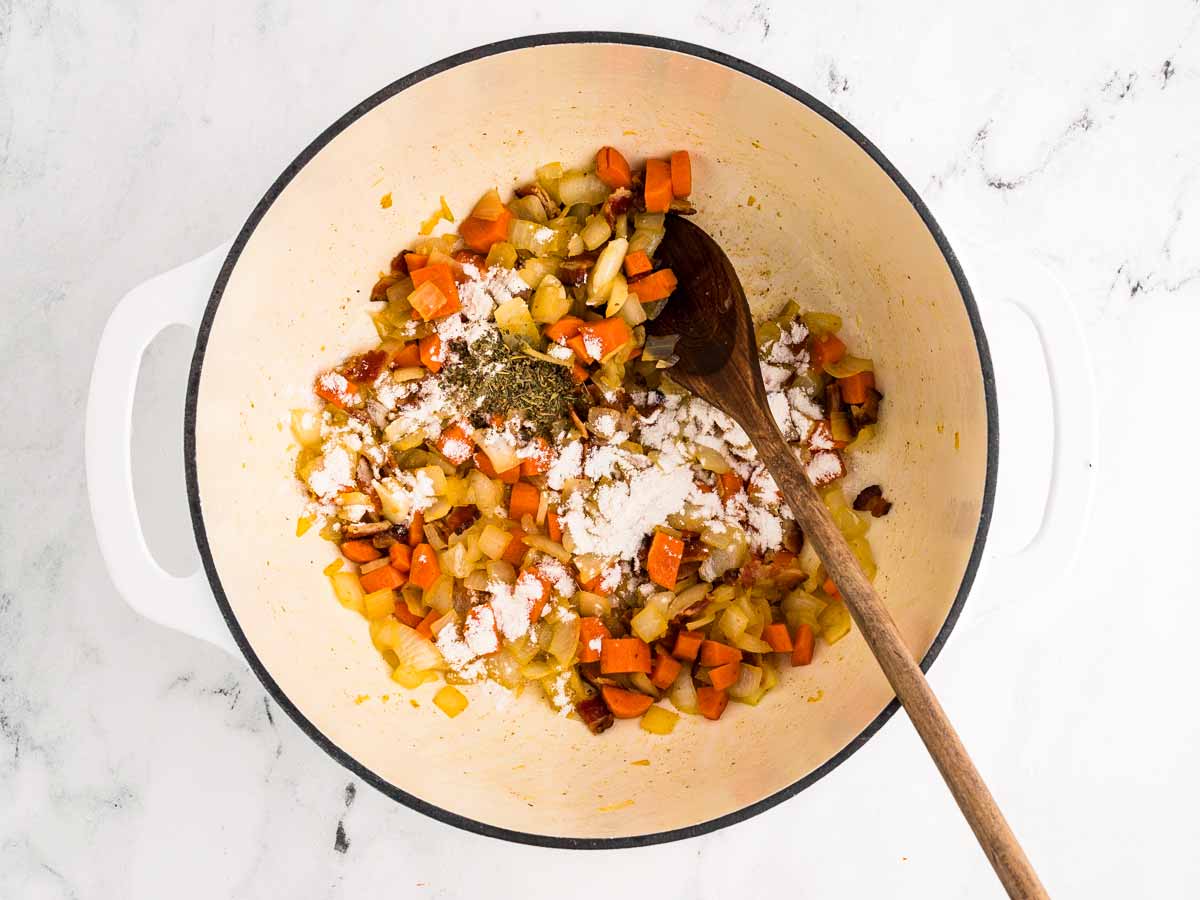 overhead view of flour and italian seasoning sprinkled over sautéed vegetables in pot