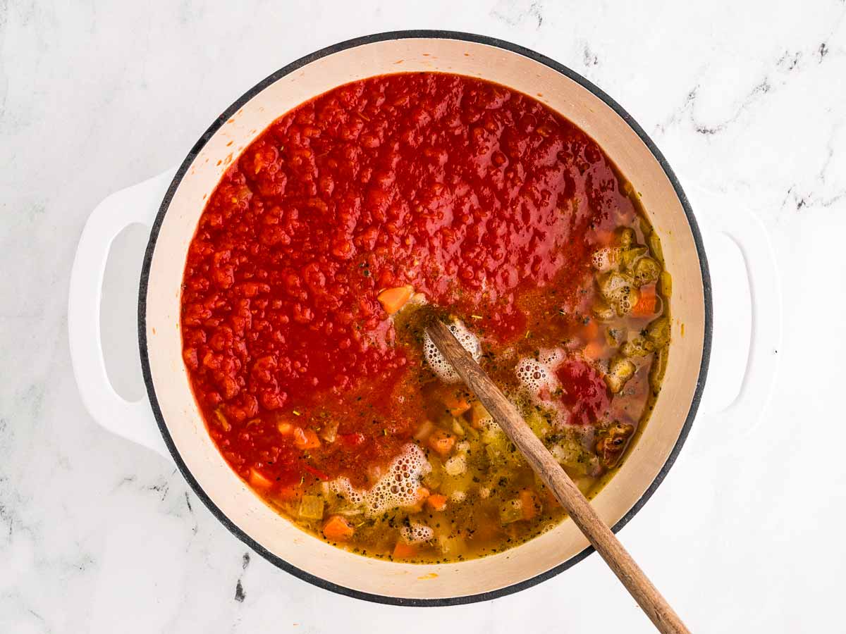 overhead view of crushed tomatoes being added to pot with broth and vegetables