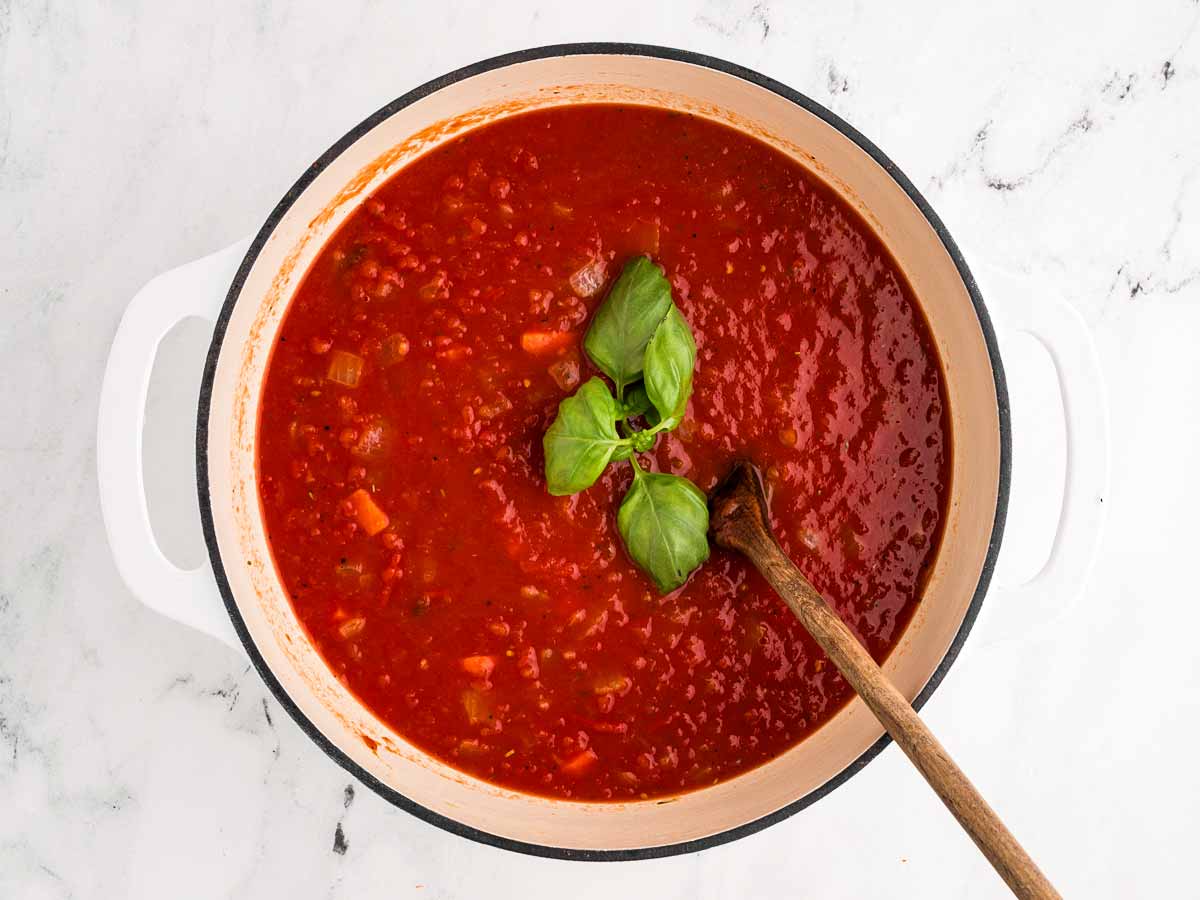 overhead view of a large stalk of fresh basil placed in the simmering tomato soup