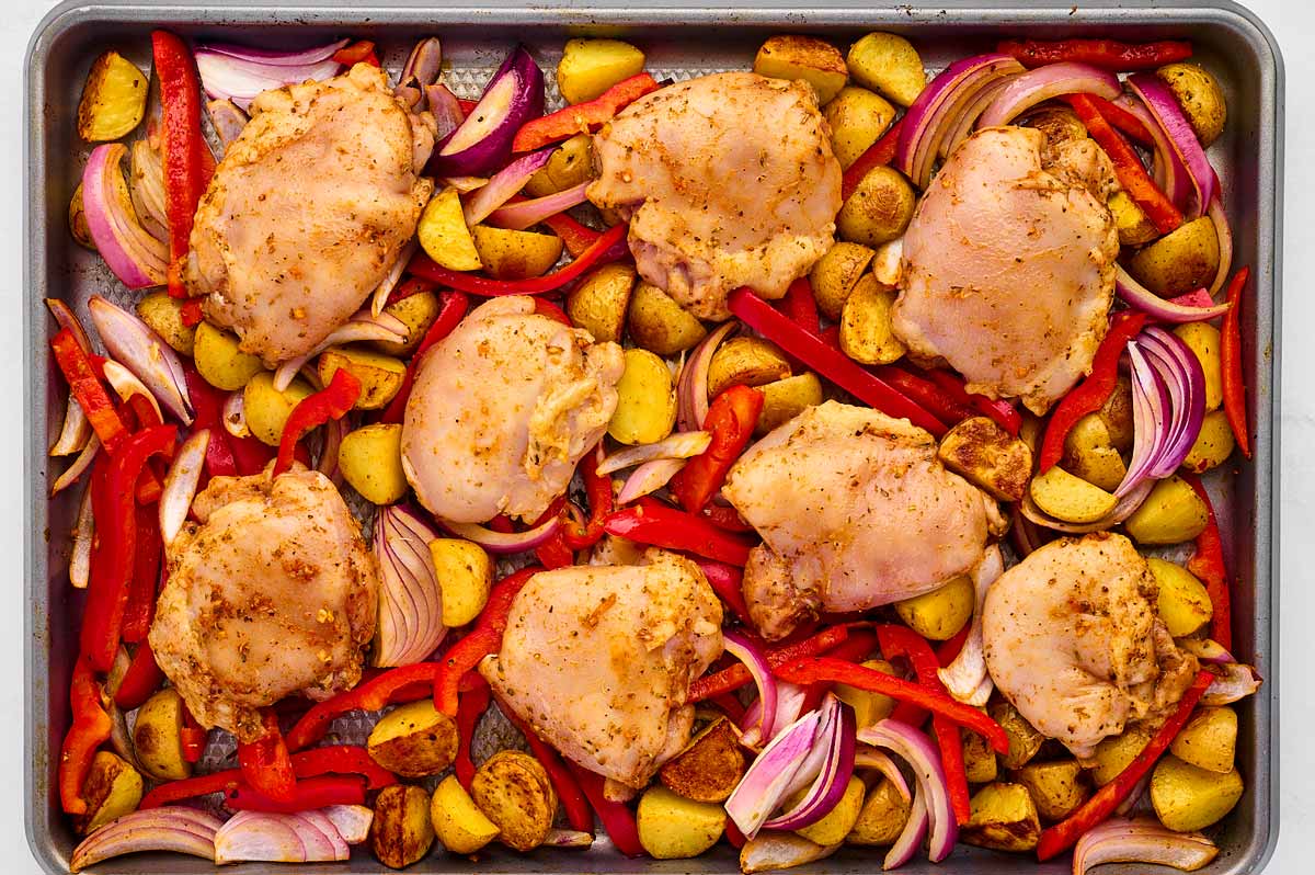 overhead view of raw seasoned chicken thighs and vegetables on sheet pan