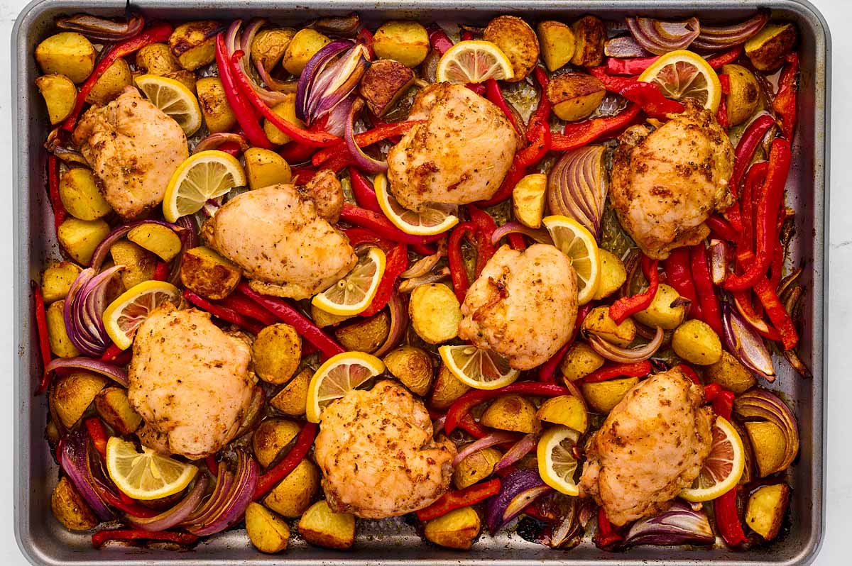 overhead view of roasted seasoned chicken thighs and vegetables on sheet pan