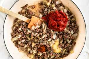 overhead view of browned ground beef with onion and tomato paste in white skillet