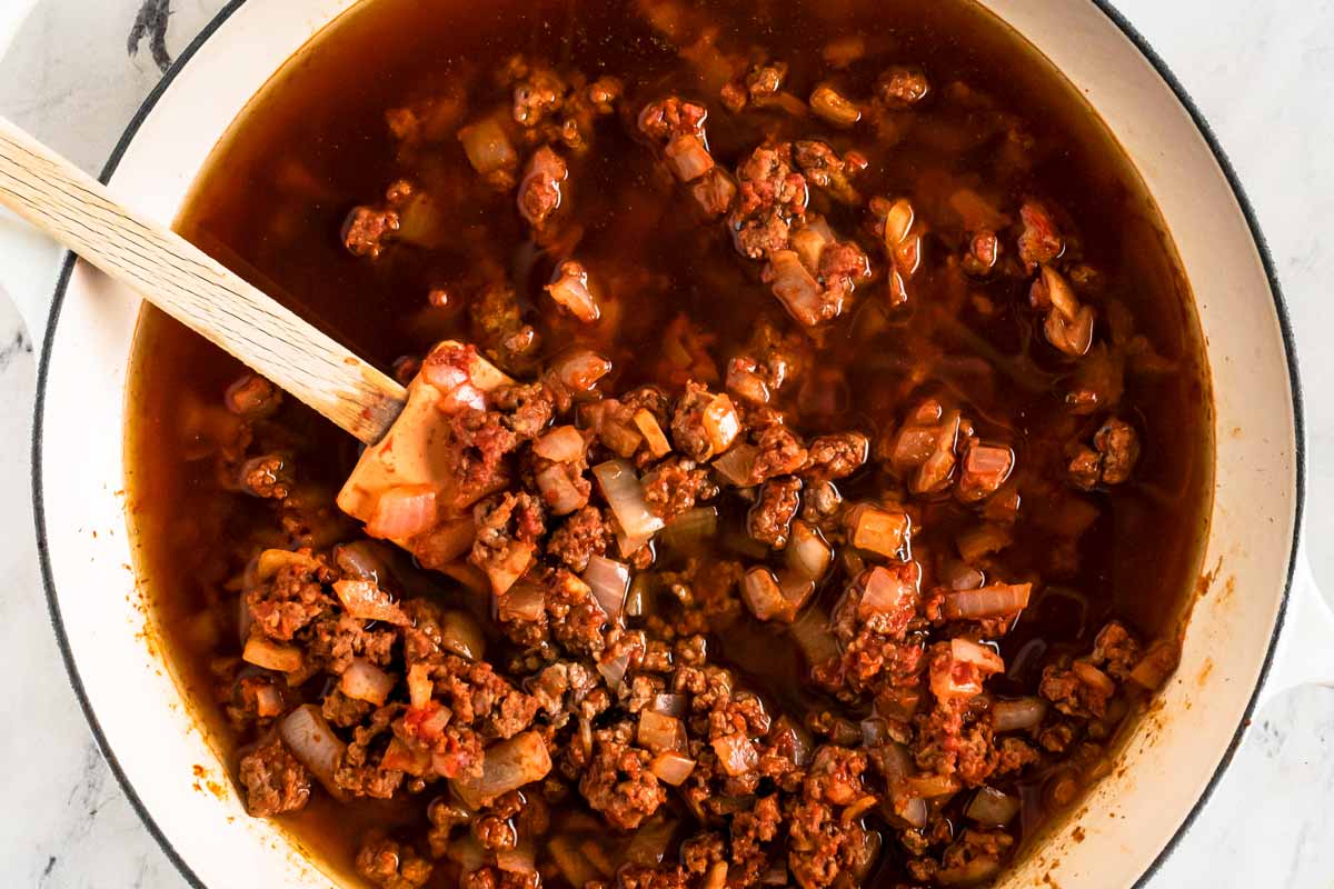 overhead view of browned ground beef with onion and broth in white skillet