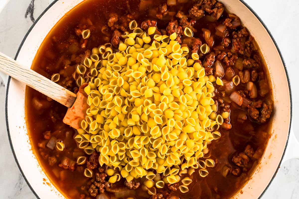 overhead view of browned ground beef with uncooked macaroni and broth in white skillet