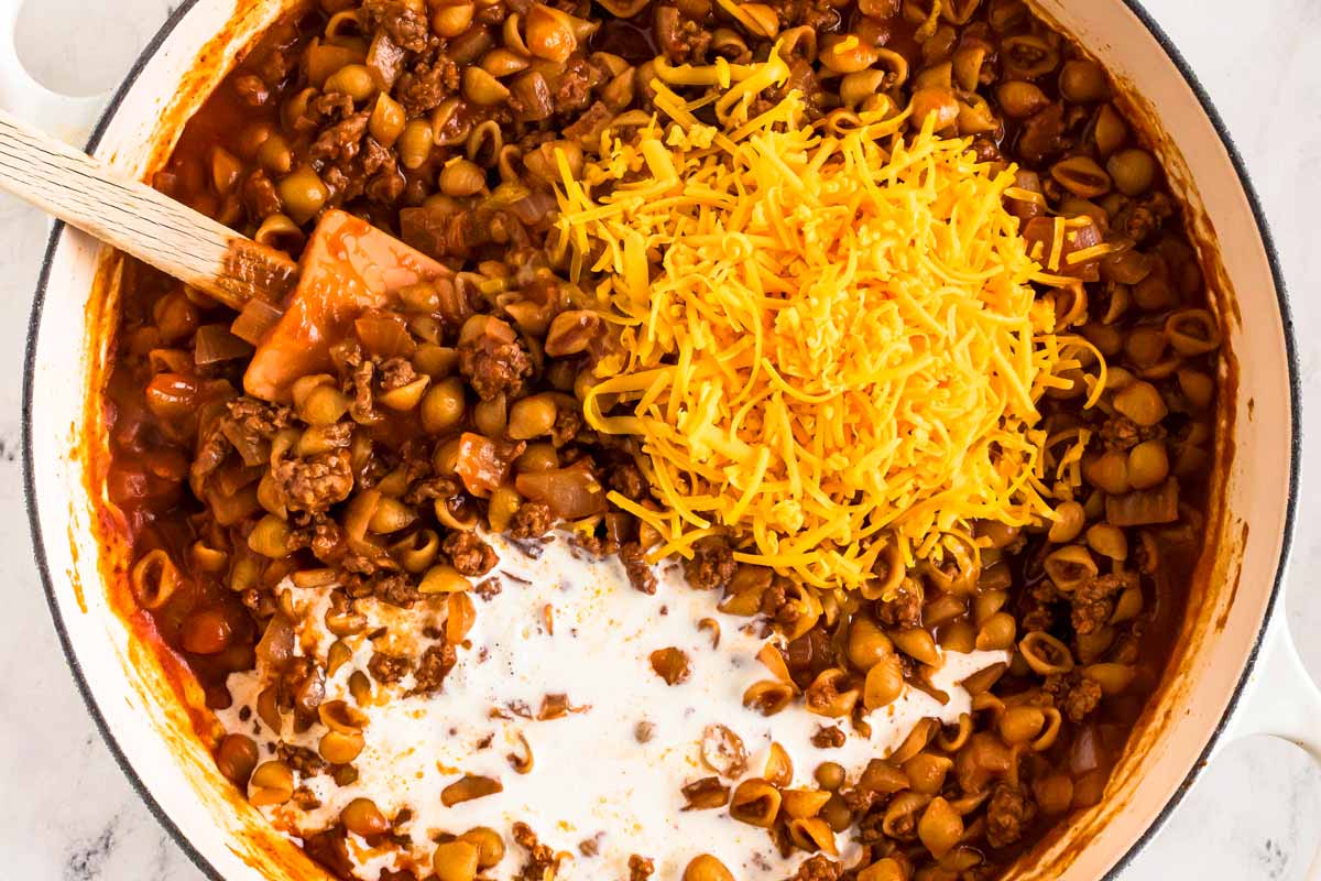 overhead view of ground beef with cooked macaroni and topped with cheese in white skillet