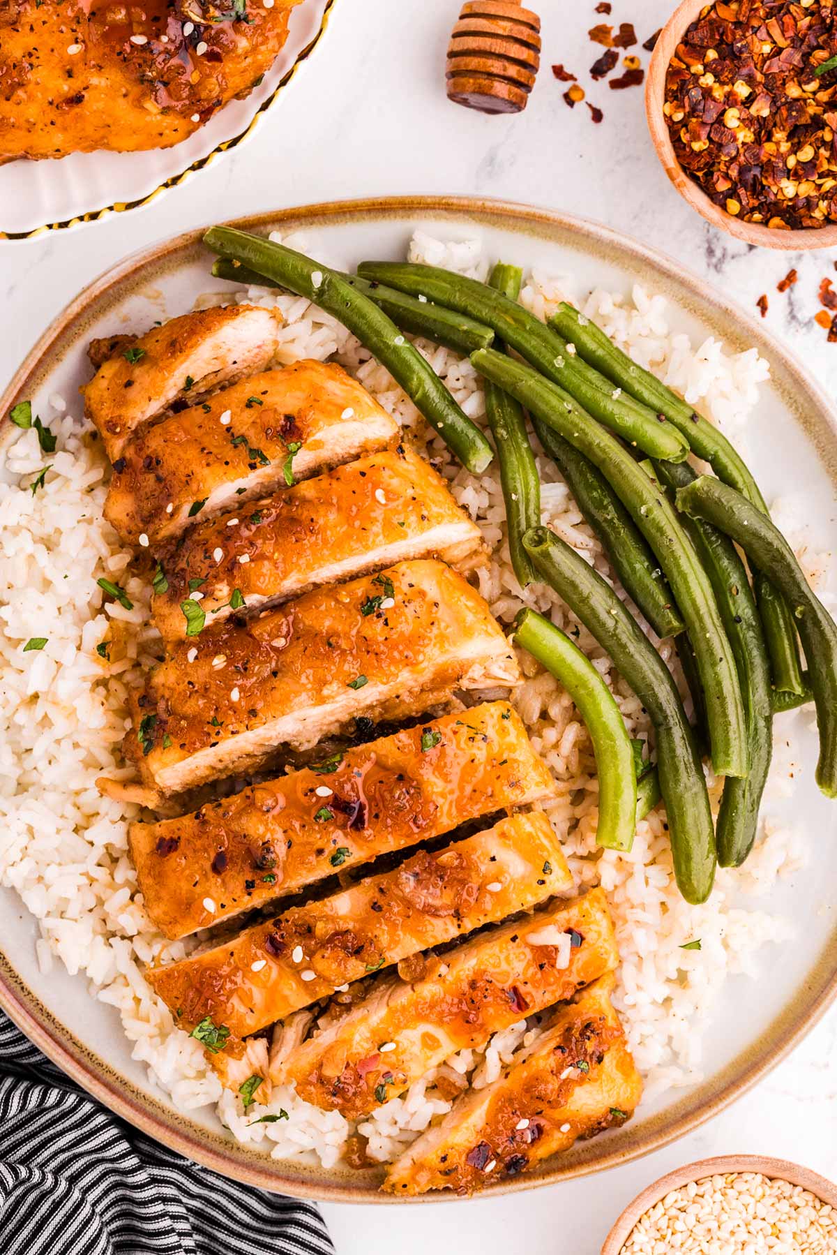 overhead view of sliced honey garlic chicken breast on plate with rice and green beans