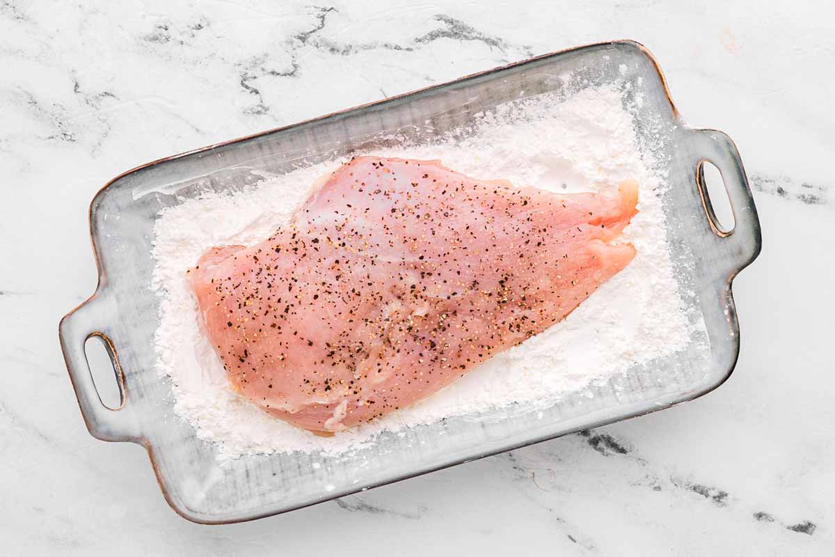 overhead view of seasoned chicken breast in bowl with cornstarch