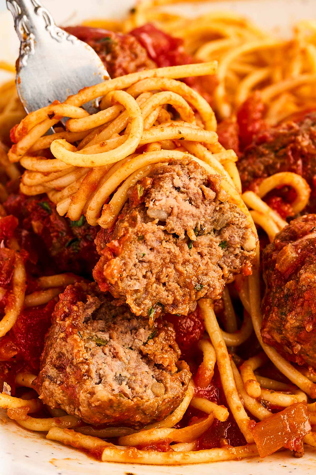 frontal close up of halved meatball on fork with spaghetti