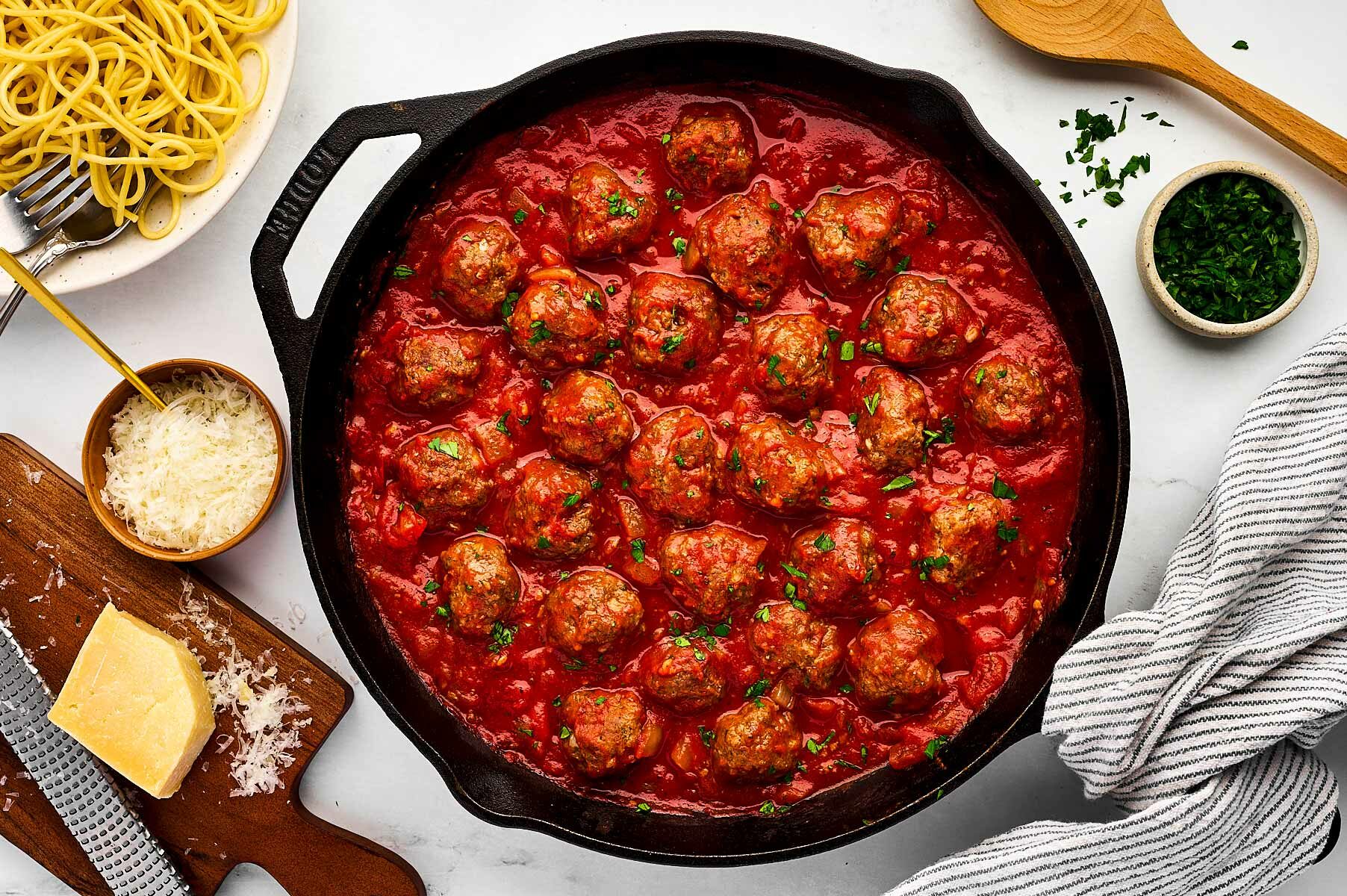 overhead view of meatballs in skillet with tomato sauce surrounded by cheese and parsley