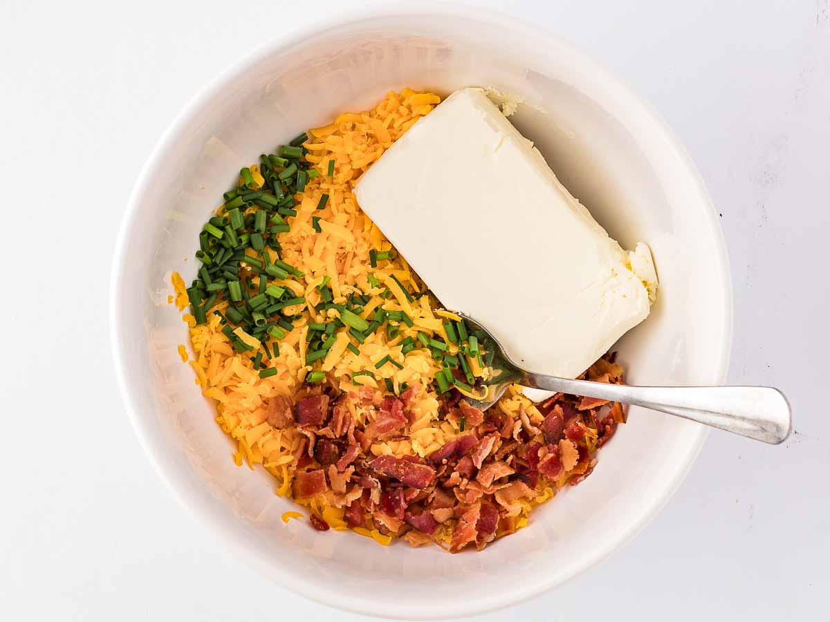 overhead view of softened cream cheese cheddar cheese chives and seasonings in a mixing bowl