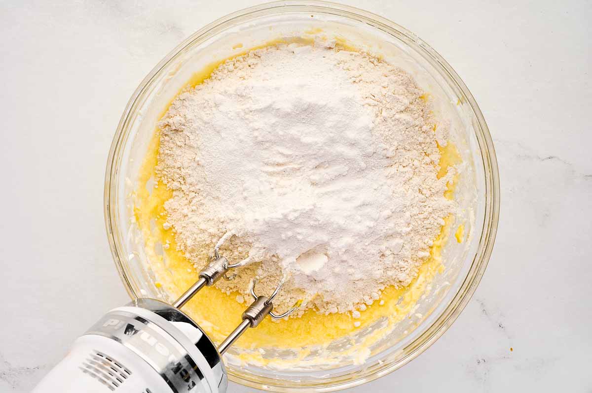 overhead view of creamy butter sugar egg mixture in bowl with flour on top