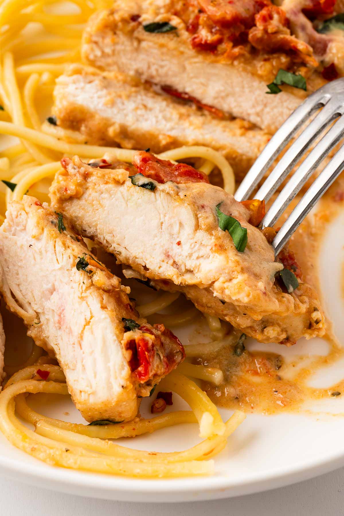 frontal close up view of sliced marry me chicken with spaghetti on plate