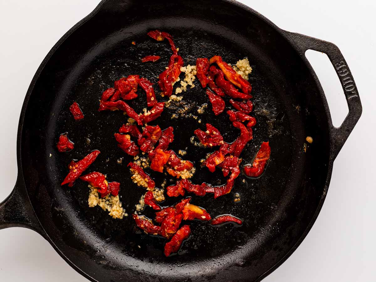 overhead view of minced garlic added to sun-dried tomatoes in skillet