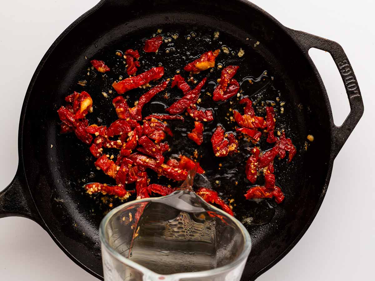 overhead view of white wine deglazing skillet with sun-dried tomatoes and garlic