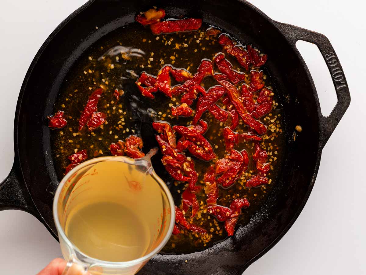 overhead view of chicken broth added to skillet with simmering sauce