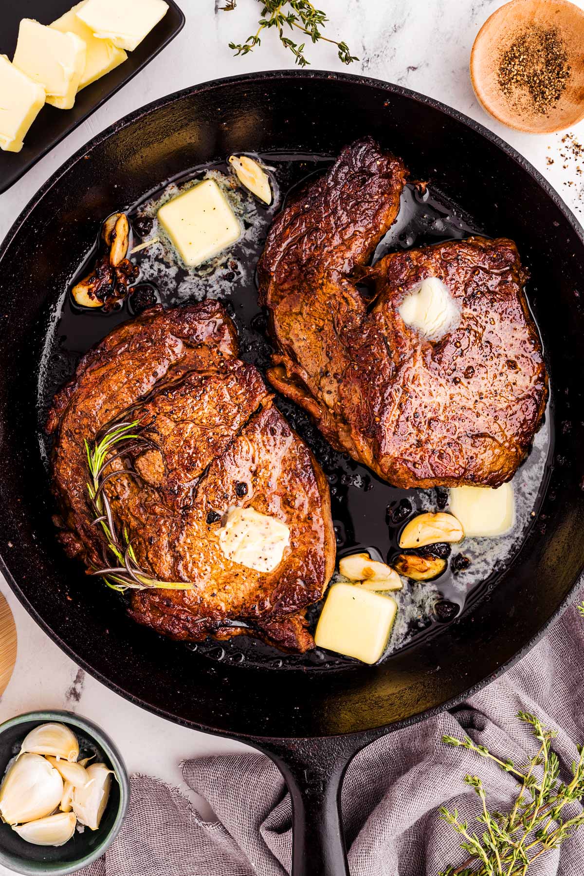 overhead view of seared steaks in cast iron skillet with butter, garlic and herbs