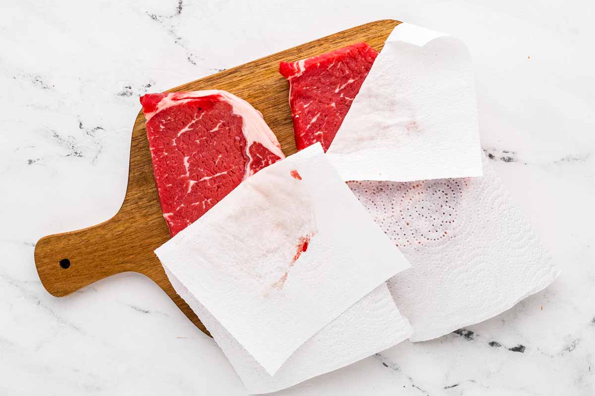 overhead view of steaks being patted dry with paper towels