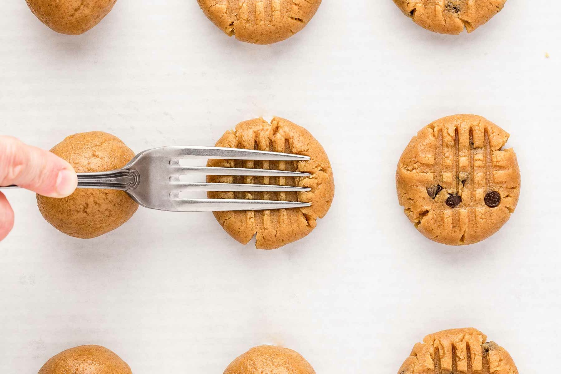 fork pressing down on peanut butter cookie to create criss cross pattern