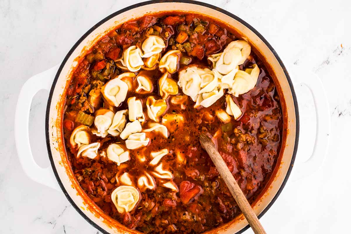 overhead view of soup with uncooked tortellini in pot