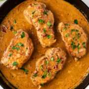 overhead view of four pork chops smothered in gravy in cast iron skillet