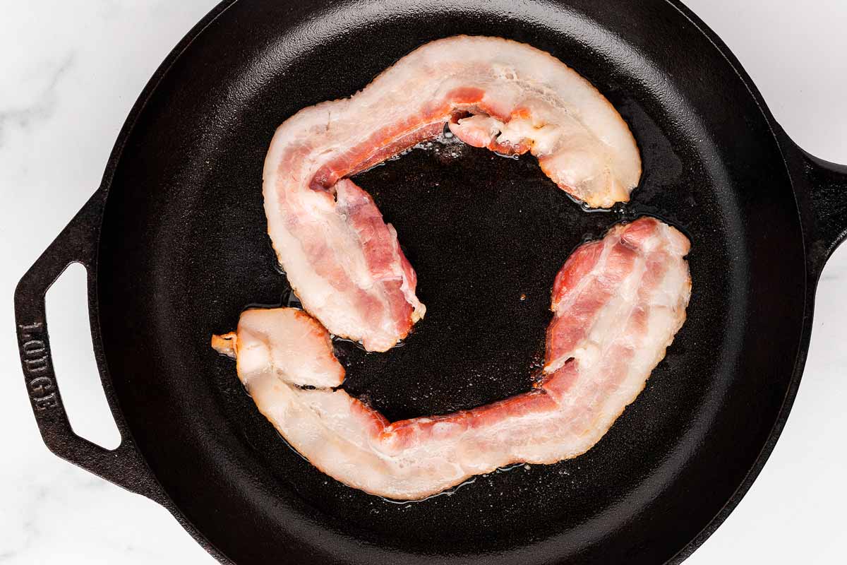 overhead view of uncooked bacon slices in cast iron skillet