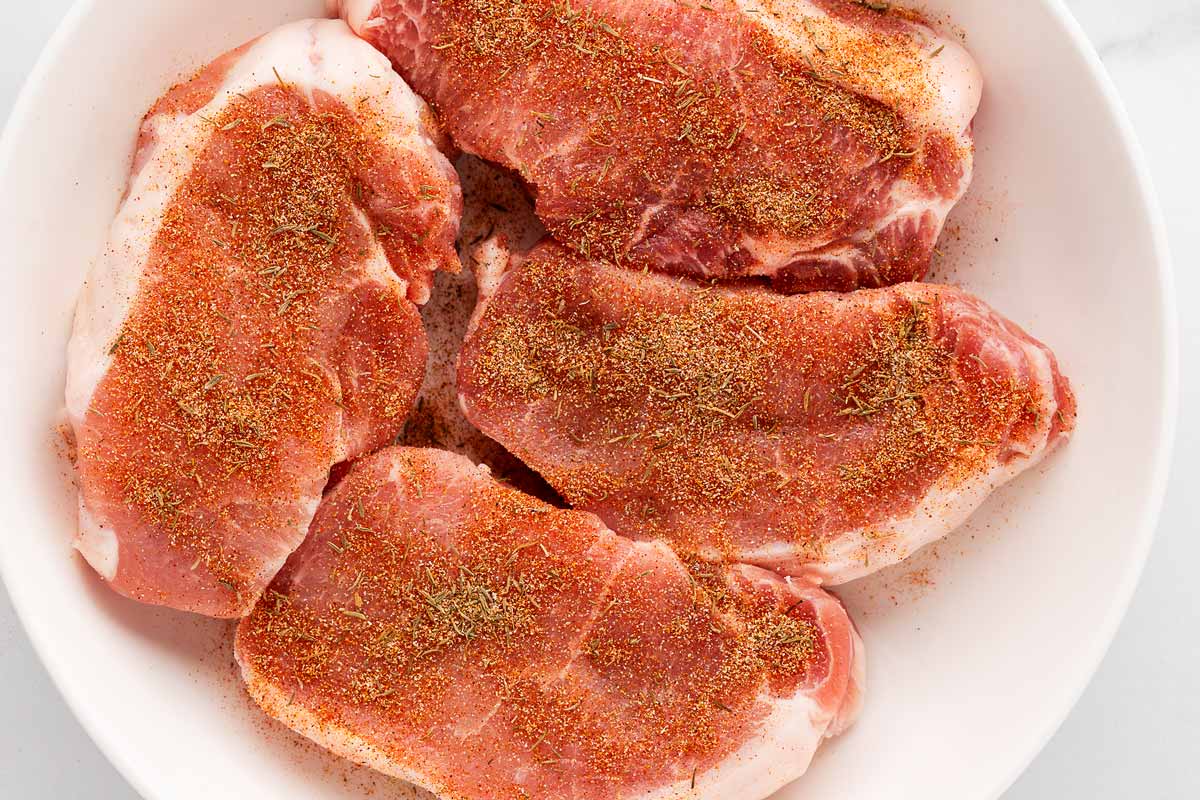 overhead view of seasoned pork chops on a plate, ready for cooking