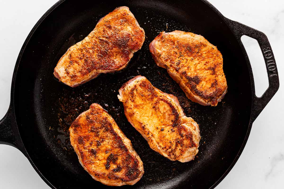 close-up of pork chops searing in a skillet, golden brown crust forming