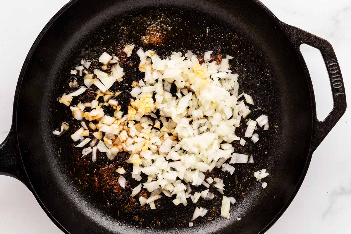 overhead view of onions and garlic sautéing in butter in a cast iron skillet