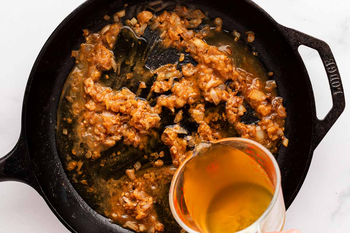 overhead view of white wine deglazing the skillet filled with browned onion