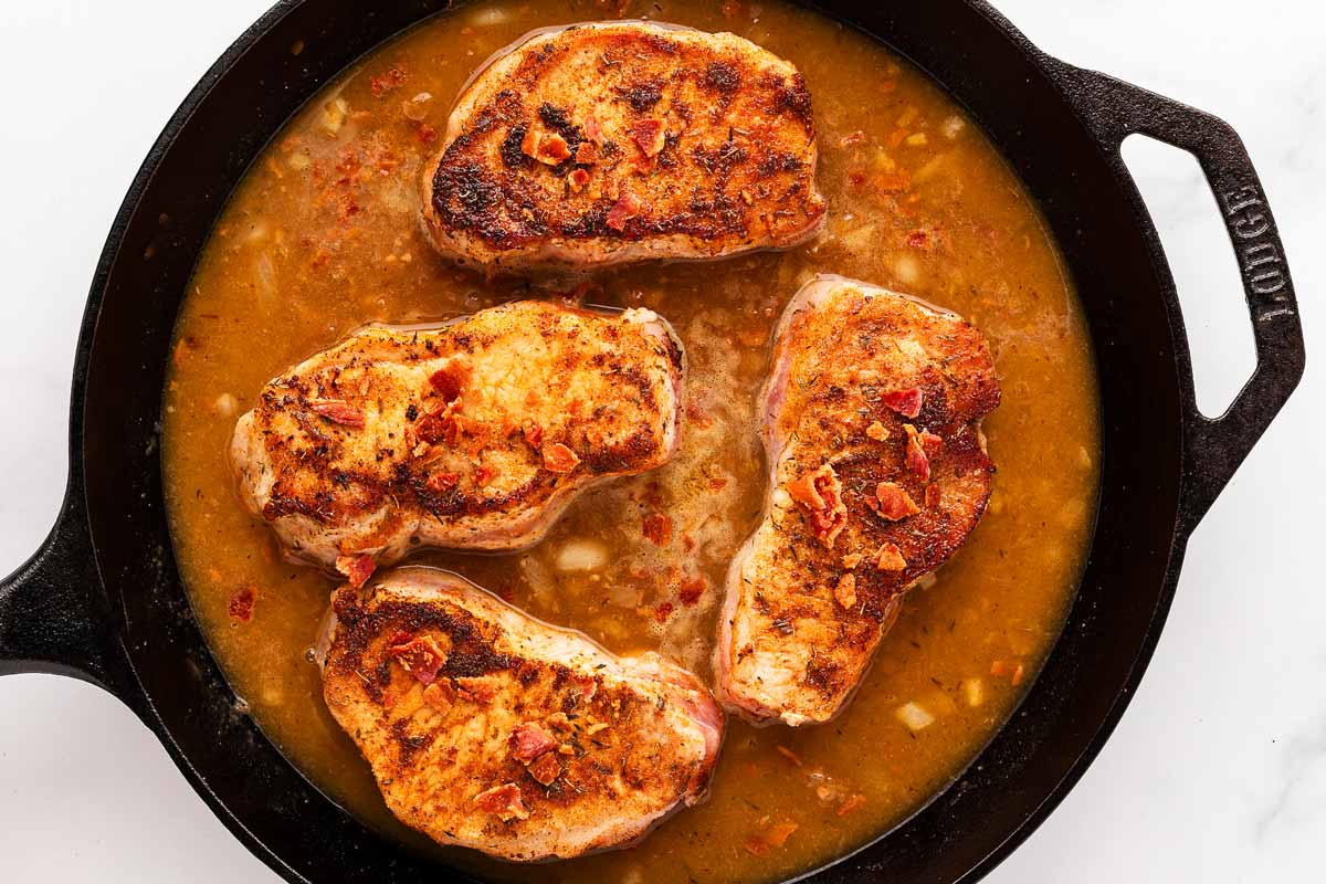 overhead view of pork chops and crispy bacon simmering in the thickened gravy