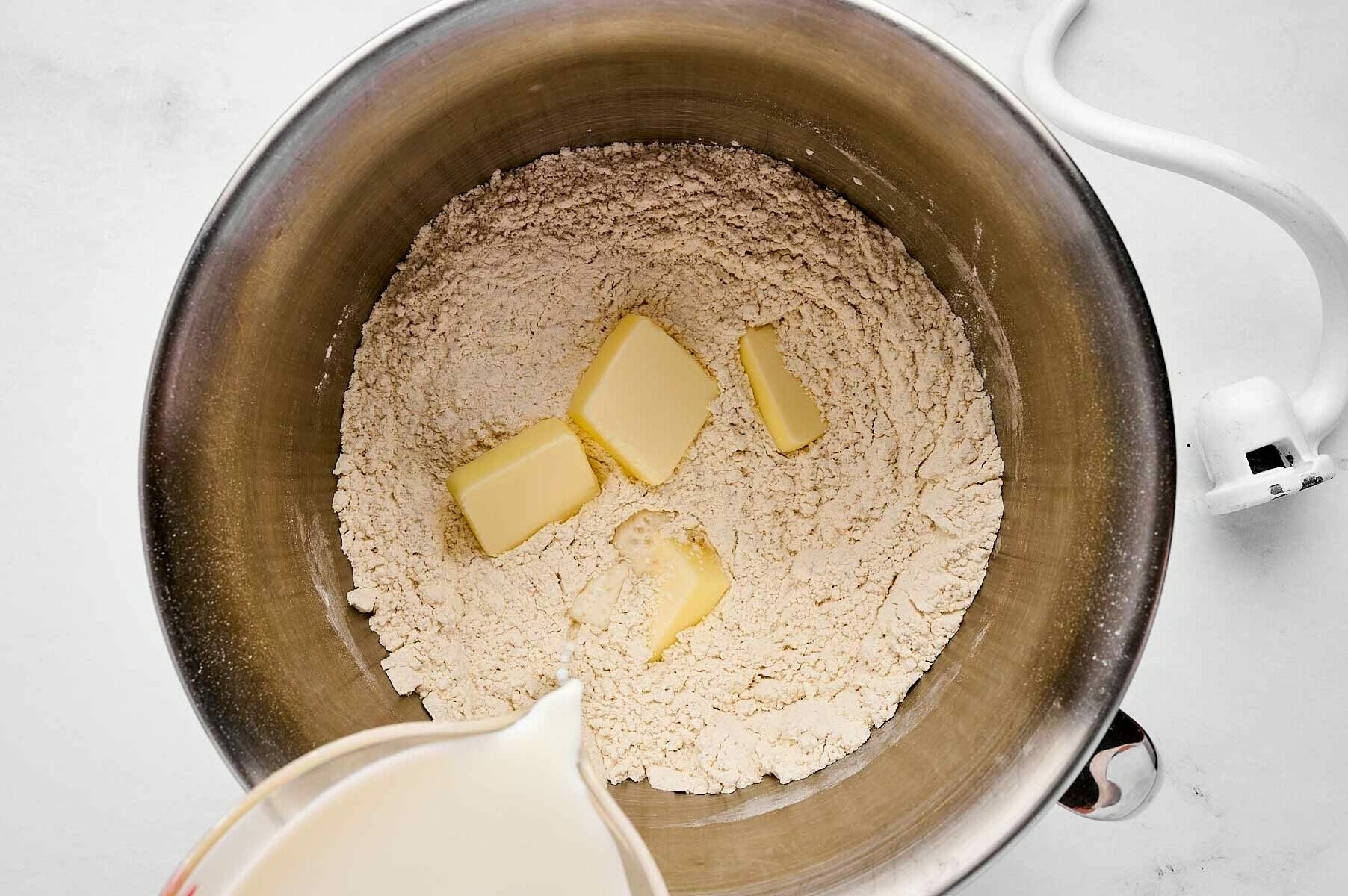 overhead view of butter and milk being added to dry ingredients in mixer bowl