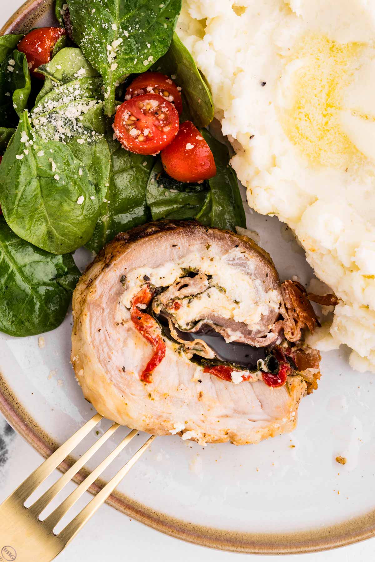 overhead view of stuffed pork loin on plate with salad and potatoes