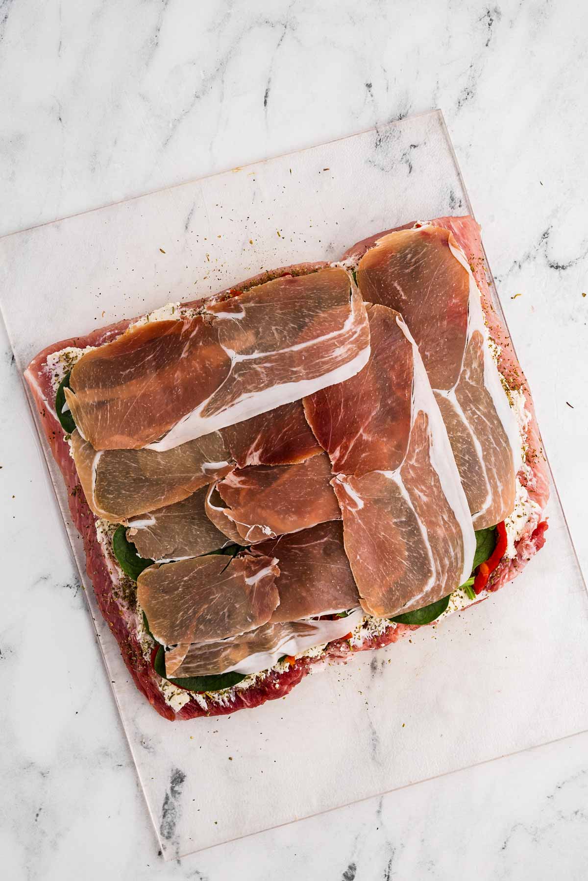 overhead view of butterflied pork loin topped with spinach and prosciutto