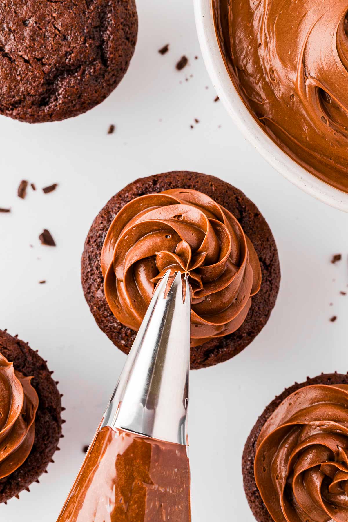 overhead view of piping bag piping whipped ganache on chocolate cupcake