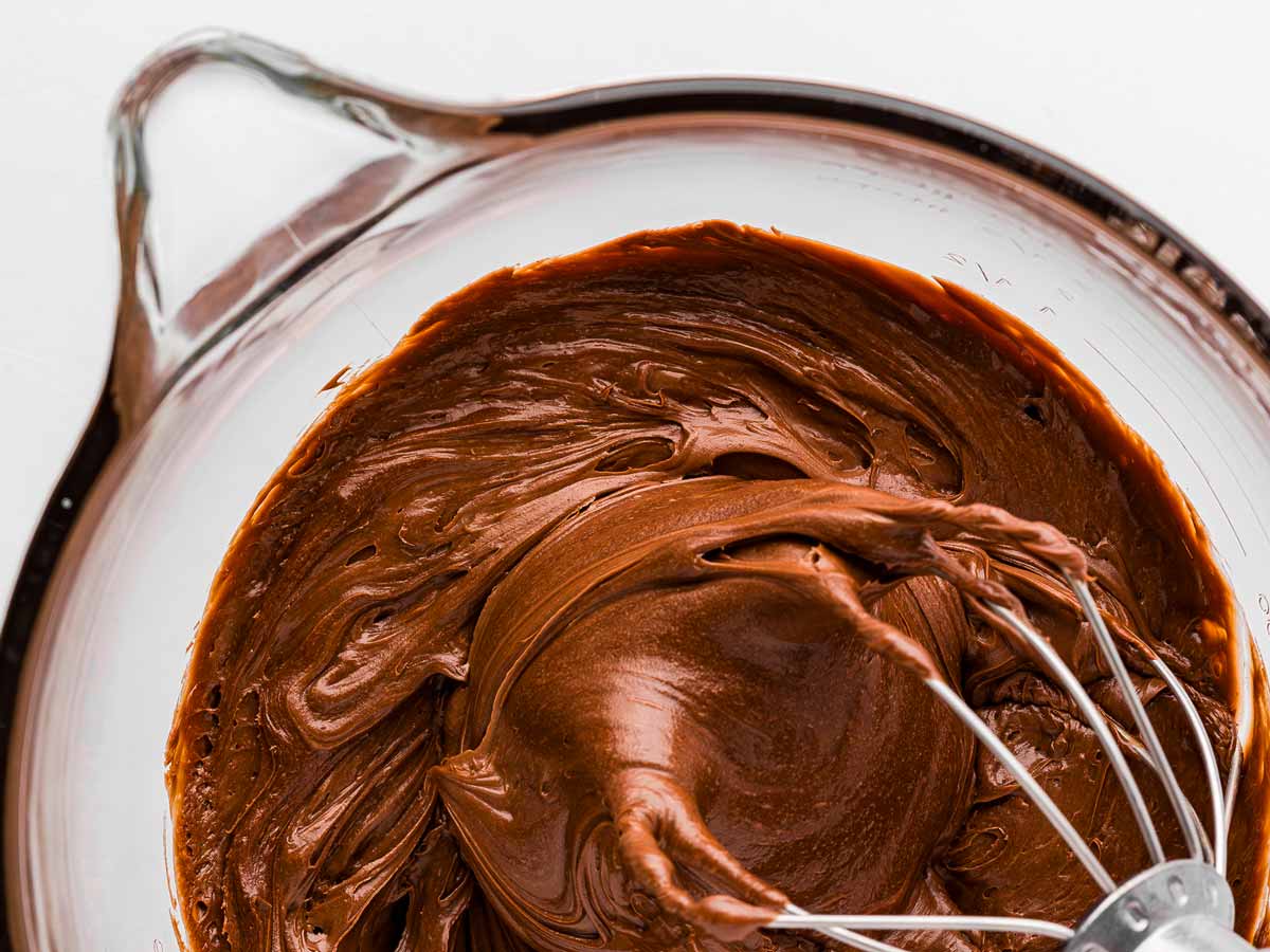 overhead view of whipped ganache in glass bowl with whisk attachment